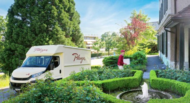 Paketzusteller vor Gebäude mit Garten Paketzusteller vor Gebäude mit Garten