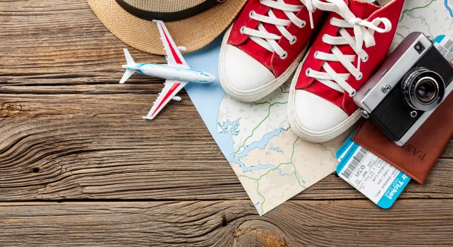 Holzdielen, darauf Sneaker, Fotokamera, Pass, Strohut, Flugtickets, kleines Flugzeit