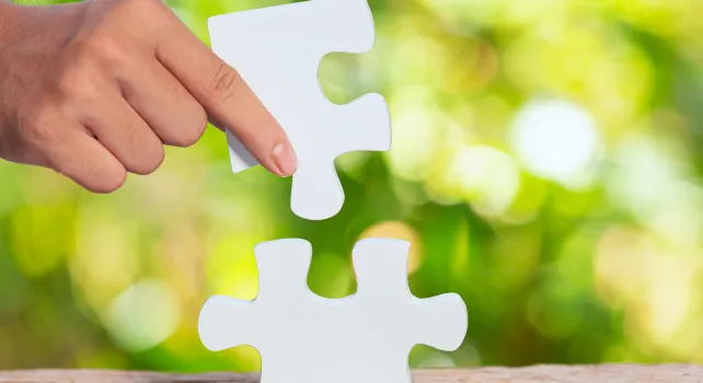 Das Bild zeigt ein Puzzle, das eine Hand zusammensetzt