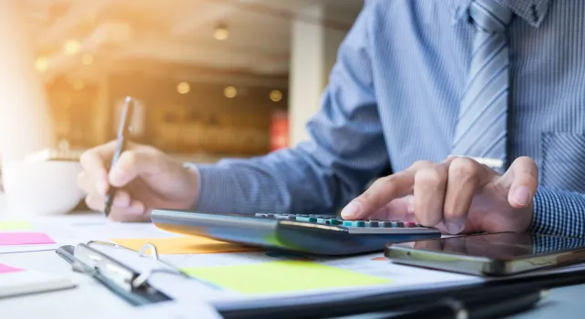 Person im Büro, arbeitet am Schreibtisch mit Taschenrechner 