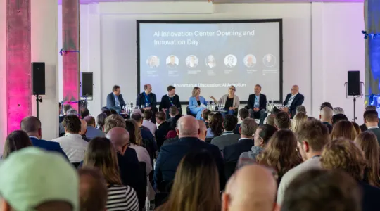 Gut gefüllter Saal mit Sicht auf sieben Referenten