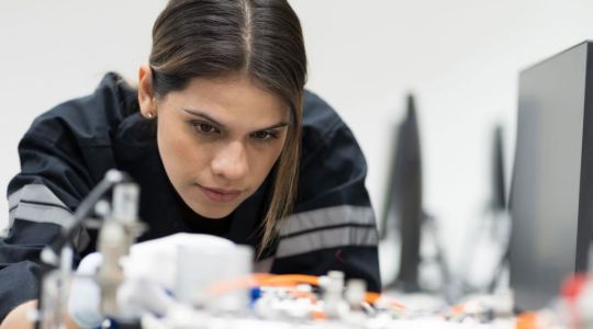 Das Bild zeigt eine junge Frau beim Löten vor technischen Geräten