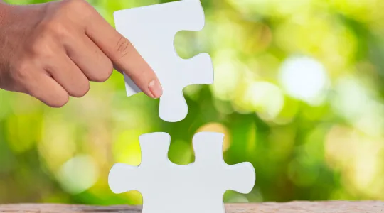 Das Bild zeigt ein Puzzle, das eine Hand zusammensetzt