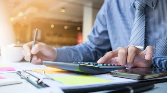 Person im Büro, arbeitet am Schreibtisch mit Taschenrechner 