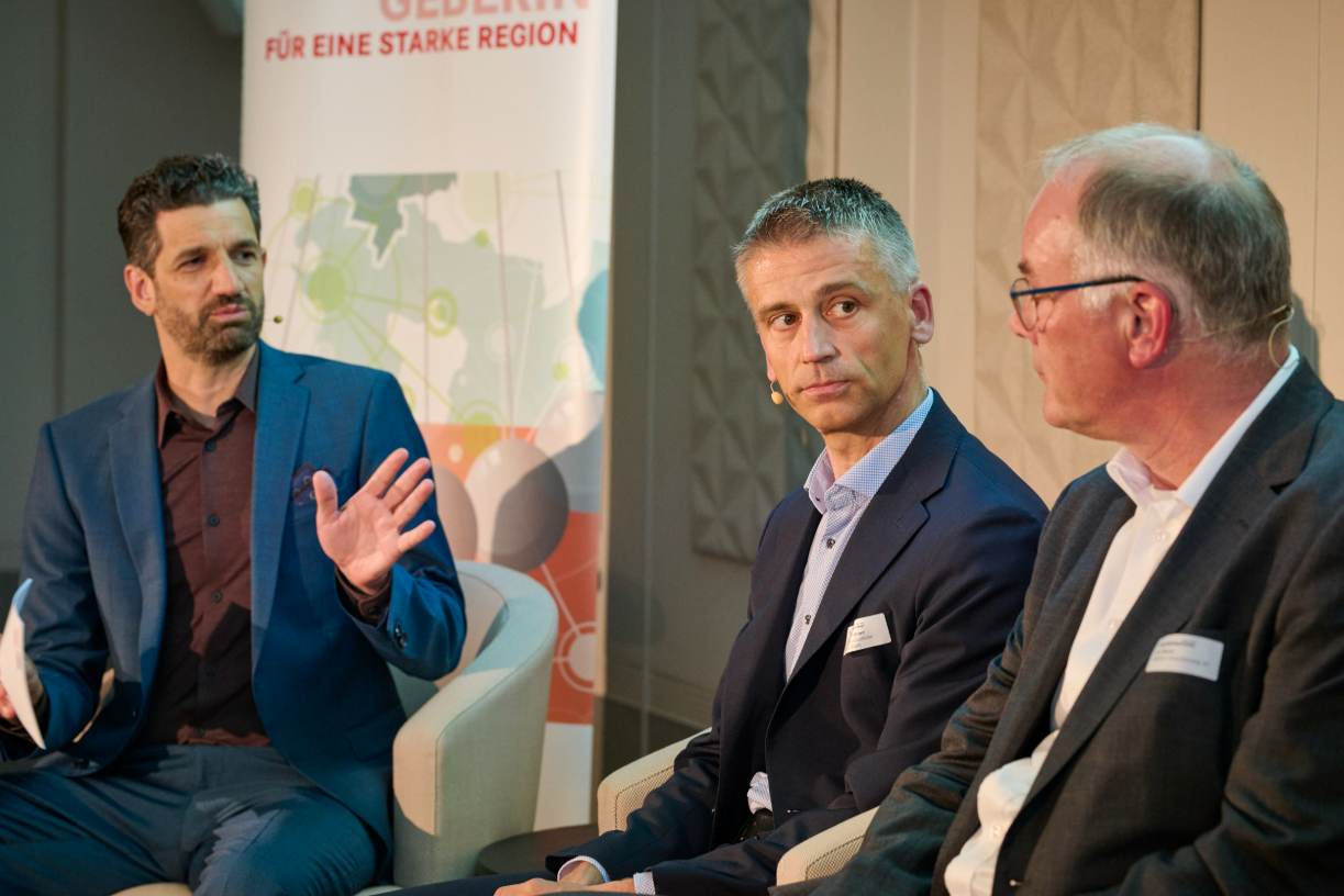 Podiumsteilnehmende Moderator Andi Lüscher diskutiert mit zwei Podiumsteilnehmenden