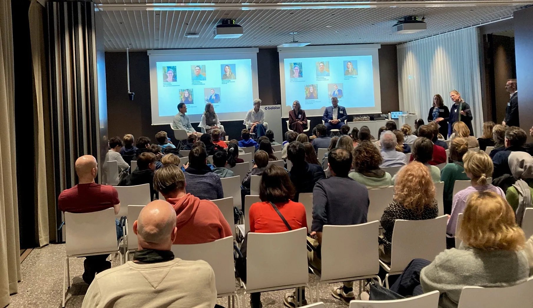 Das Bild zeigt sitzende Eltern und Kinder, die der Podiumsdiskussion zuhören 