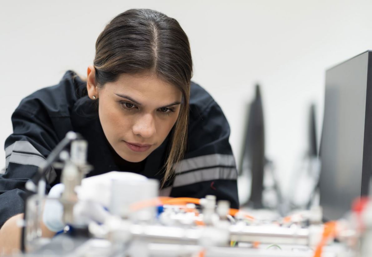 Das Bild zeigt eine junge Frau beim Löten vor technischen Geräten