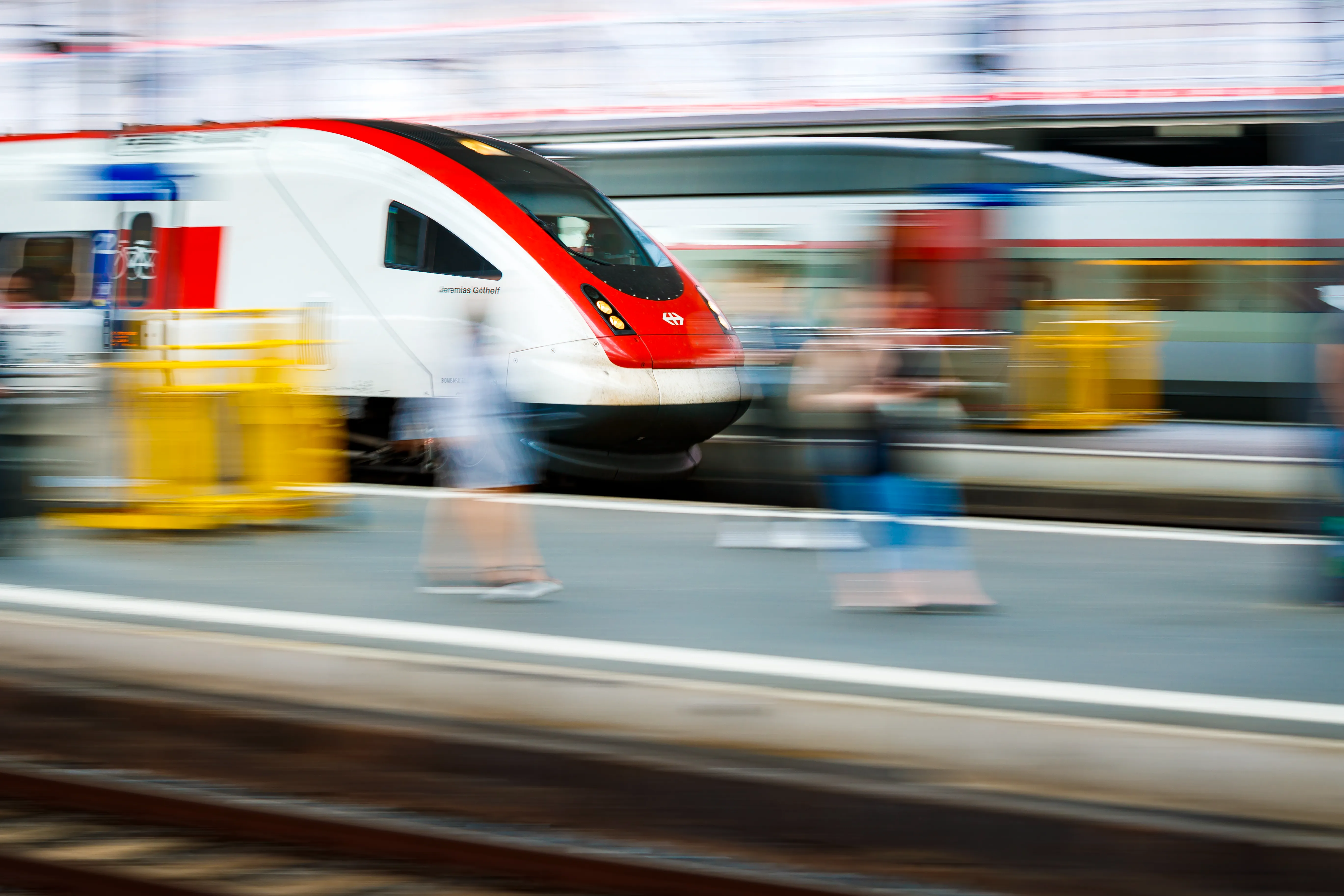 Das Bild zeigt einen Zug und ein Bahngleis mit Menschen.